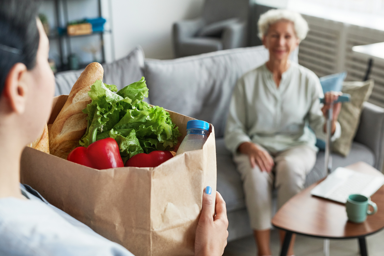 A volunteer delivering a bag of groceries to a smiling older woman at home